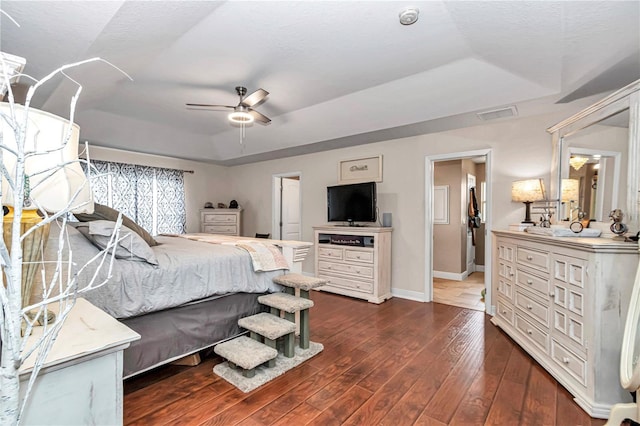 bedroom featuring ceiling fan, visible vents, baseboards, dark wood-style floors, and a tray ceiling