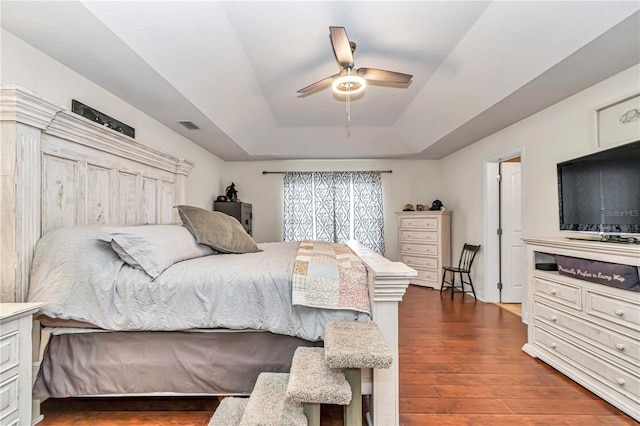 bedroom with ceiling fan, a tray ceiling, dark wood-type flooring, and visible vents