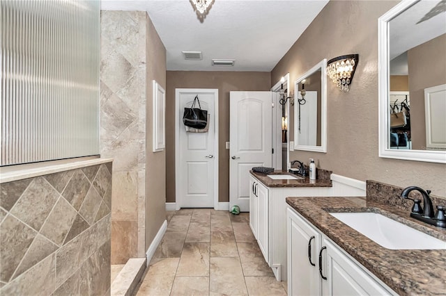 bathroom with a tile shower, visible vents, two vanities, and a sink