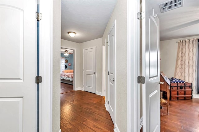 hall featuring dark wood-type flooring, visible vents, and baseboards