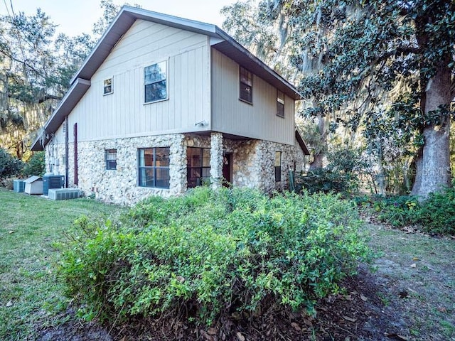 view of property exterior featuring stone siding, a yard, and central air condition unit