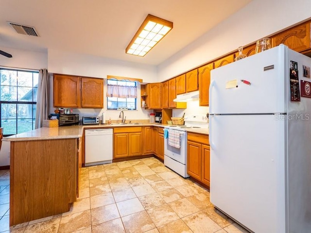 kitchen featuring white appliances, visible vents, brown cabinets, under cabinet range hood, and a sink