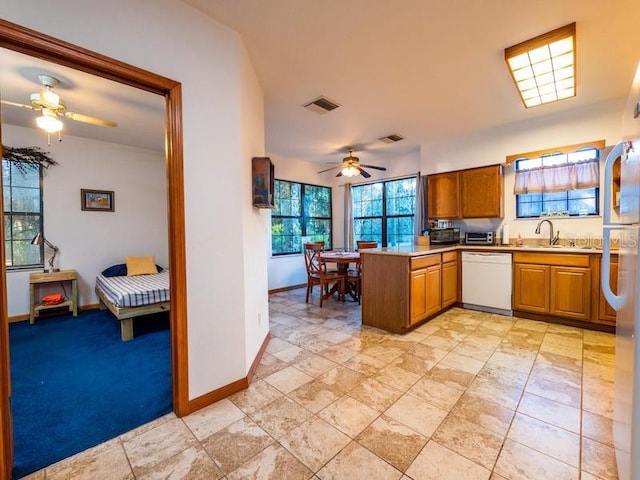 kitchen featuring brown cabinets, light countertops, white dishwasher, a sink, and a peninsula