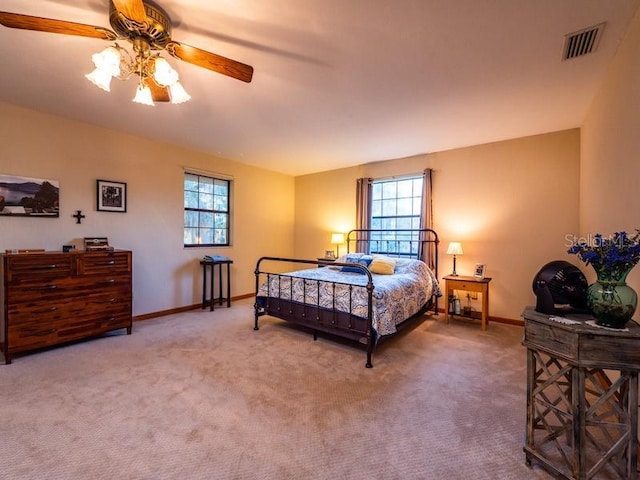 carpeted bedroom with baseboards, multiple windows, visible vents, and ceiling fan