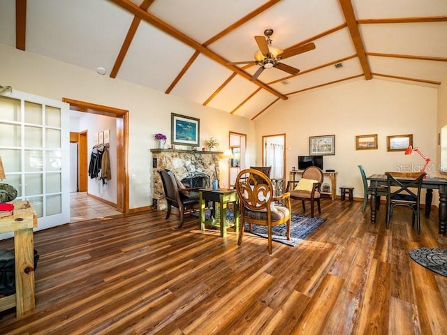 living area with high vaulted ceiling, dark wood-style flooring, ceiling fan, and a stone fireplace