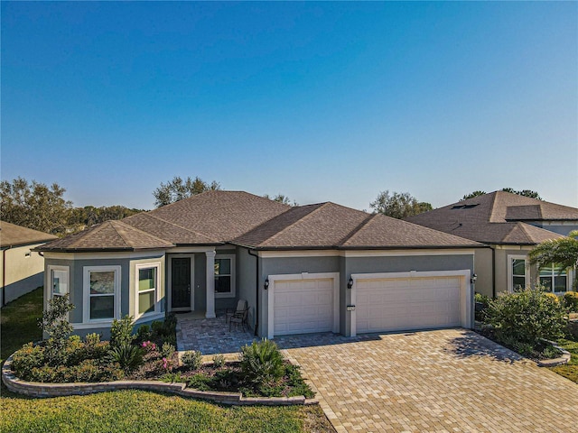 ranch-style house with an attached garage, roof with shingles, decorative driveway, and stucco siding