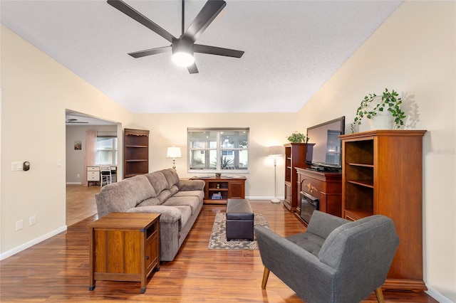 living area featuring lofted ceiling, a textured ceiling, wood finished floors, and a ceiling fan