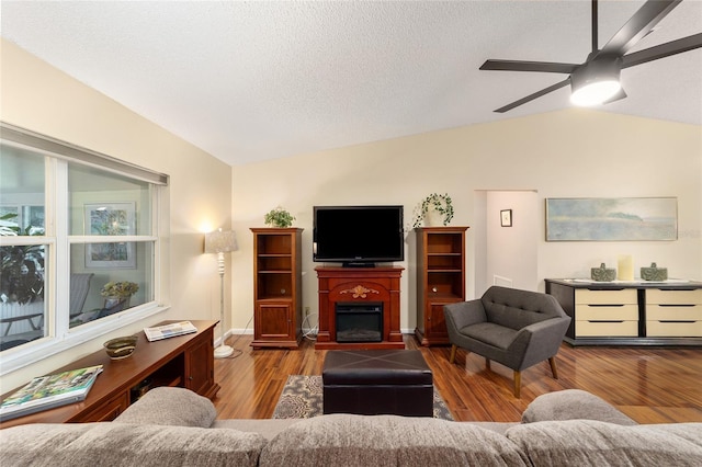 living room featuring ceiling fan, a textured ceiling, a fireplace, wood finished floors, and vaulted ceiling