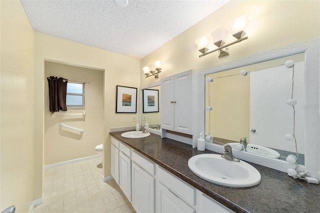 bathroom with a sink, a textured ceiling, toilet, and double vanity