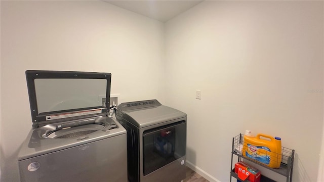 laundry room with laundry area, separate washer and dryer, wood finished floors, and baseboards