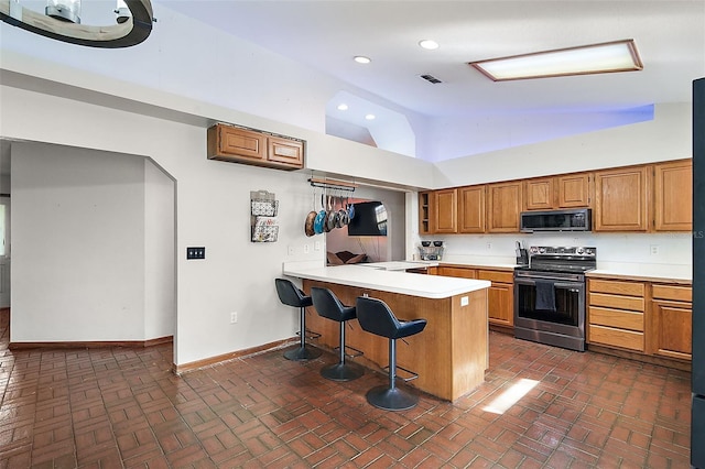 kitchen featuring a breakfast bar, light countertops, stainless steel range with electric stovetop, black microwave, and a peninsula