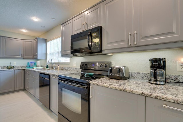 kitchen with gray cabinets, a sink, black appliances, and light stone countertops