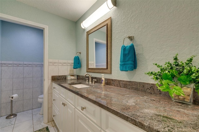 bathroom featuring tile walls, a textured wall, toilet, vanity, and a textured ceiling