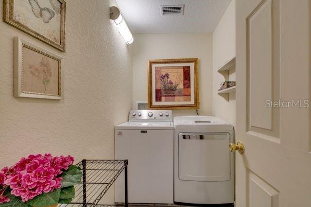 clothes washing area featuring a textured ceiling, a textured wall, laundry area, visible vents, and washer and dryer