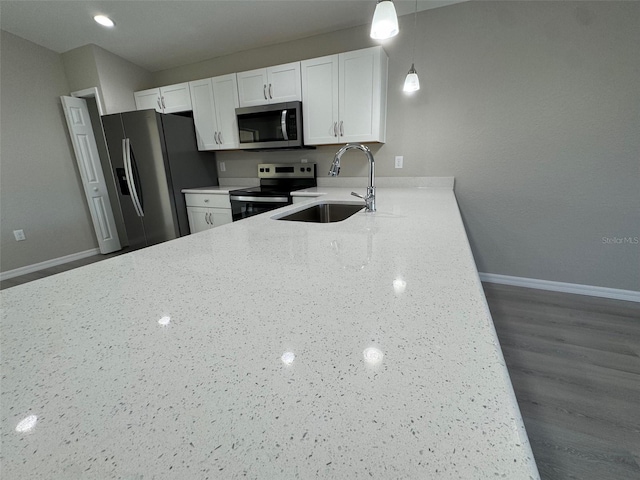 kitchen with hanging light fixtures, appliances with stainless steel finishes, white cabinetry, a sink, and light stone countertops