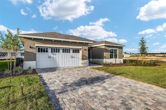 prairie-style home with a front yard, decorative driveway, an attached garage, and stucco siding