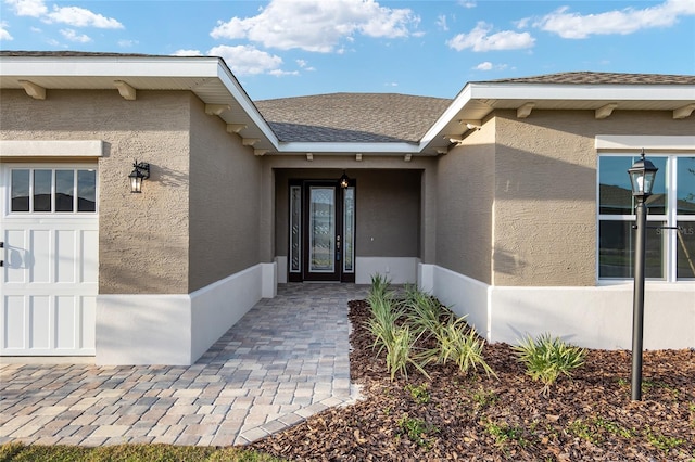 doorway to property with an attached garage, roof with shingles, and stucco siding