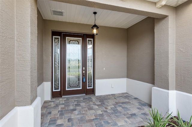 view of exterior entry with visible vents and stucco siding