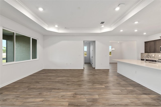 unfurnished living room featuring wood finished floors, a tray ceiling, a sink, and ornamental molding