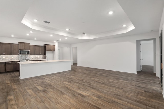 kitchen featuring visible vents, stainless steel microwave, a kitchen island with sink, a tray ceiling, and light countertops