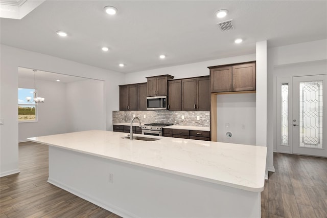 kitchen with stainless steel appliances, visible vents, a sink, an island with sink, and light stone countertops