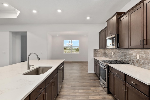 kitchen with tasteful backsplash, appliances with stainless steel finishes, light stone counters, hanging light fixtures, and a sink