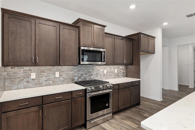 kitchen featuring appliances with stainless steel finishes, visible vents, dark brown cabinetry, and tasteful backsplash