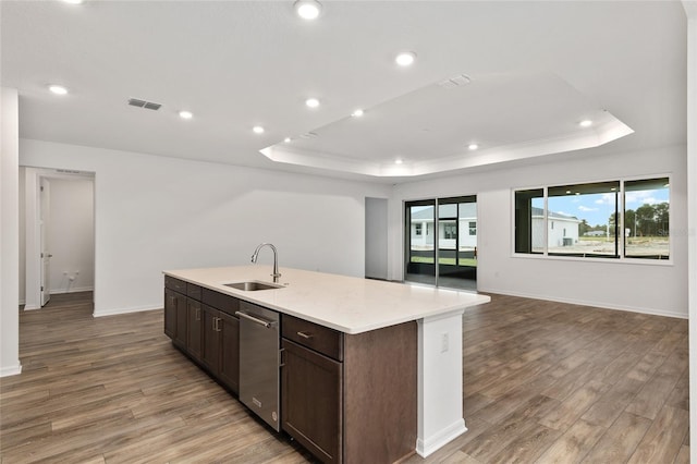 kitchen featuring a sink, wood finished floors, visible vents, an island with sink, and a raised ceiling