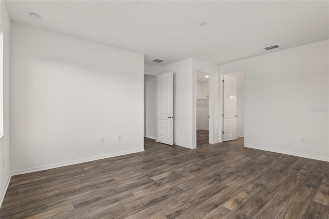 unfurnished bedroom featuring a walk in closet, dark wood-style flooring, visible vents, and baseboards