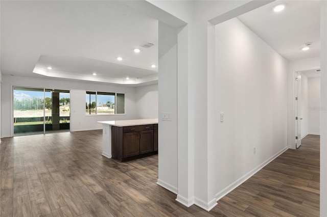 interior space with baseboards, visible vents, dark wood-type flooring, a tray ceiling, and recessed lighting