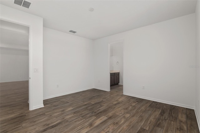 empty room featuring dark wood-style flooring, visible vents, and baseboards