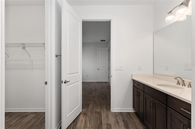 bathroom featuring a walk in closet, vanity, baseboards, and wood finished floors