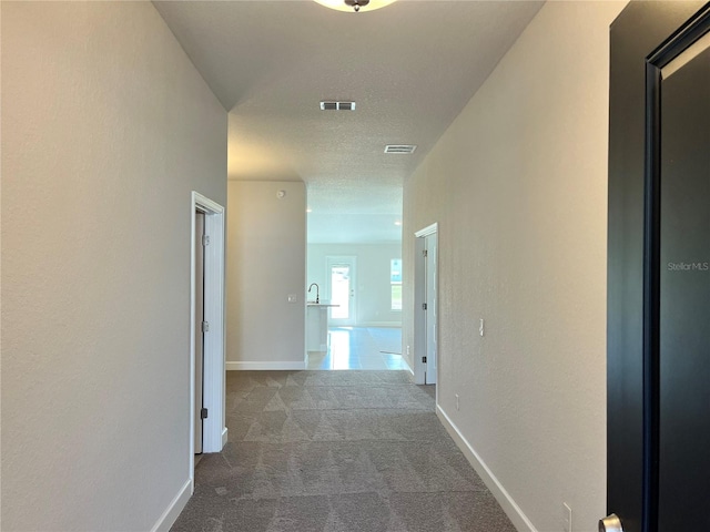 hall featuring carpet floors, visible vents, a textured ceiling, and baseboards