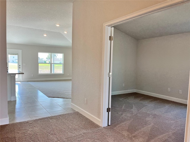 tiled spare room with carpet floors, baseboards, and a textured ceiling