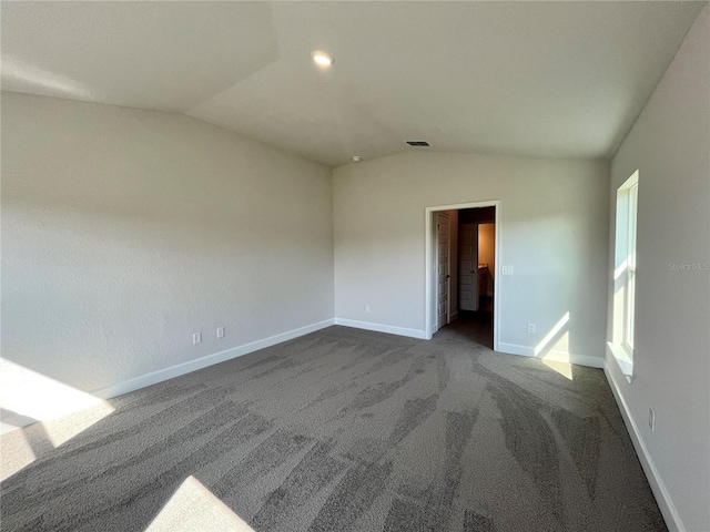 empty room with visible vents, baseboards, vaulted ceiling, and dark colored carpet