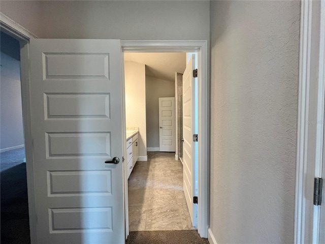 hallway featuring a textured wall and baseboards