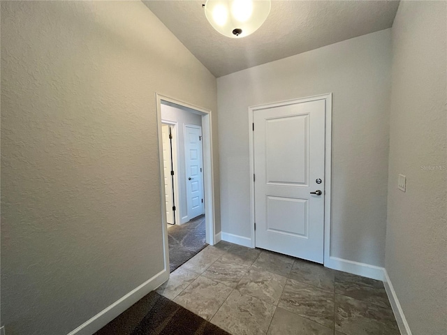 doorway to outside featuring lofted ceiling, a textured wall, and baseboards