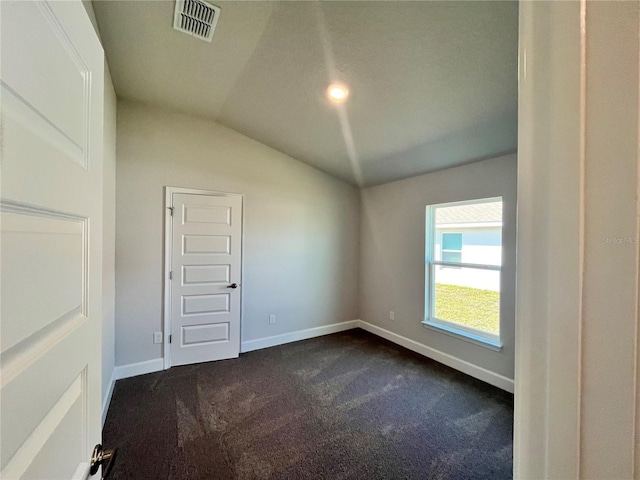 spare room with baseboards, visible vents, vaulted ceiling, and dark colored carpet