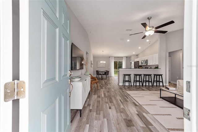 foyer with ceiling fan with notable chandelier, high vaulted ceiling, light wood finished floors, and recessed lighting