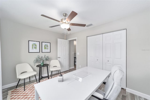 office area with a ceiling fan, visible vents, baseboards, and wood finished floors