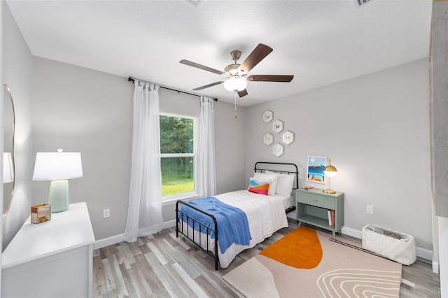 bedroom featuring a textured ceiling, light wood-type flooring, a ceiling fan, and baseboards