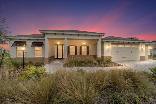 view of front of property featuring a garage, driveway, a shingled roof, and stucco siding