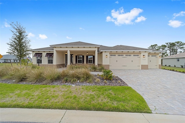 prairie-style house featuring a front lawn, decorative driveway, an attached garage, and stucco siding