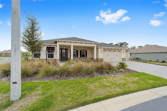 view of front of home with decorative driveway, stucco siding, a shingled roof, a front yard, and a garage