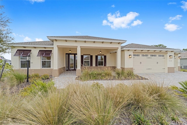 prairie-style home featuring decorative driveway, roof with shingles, an attached garage, and stucco siding