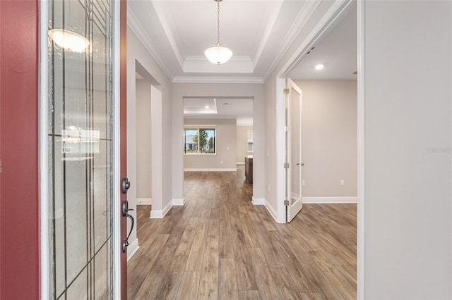 foyer with baseboards, wood finished floors, a raised ceiling, and crown molding