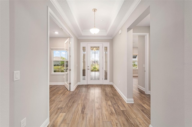 foyer featuring crown molding, light wood finished floors, a raised ceiling, and baseboards