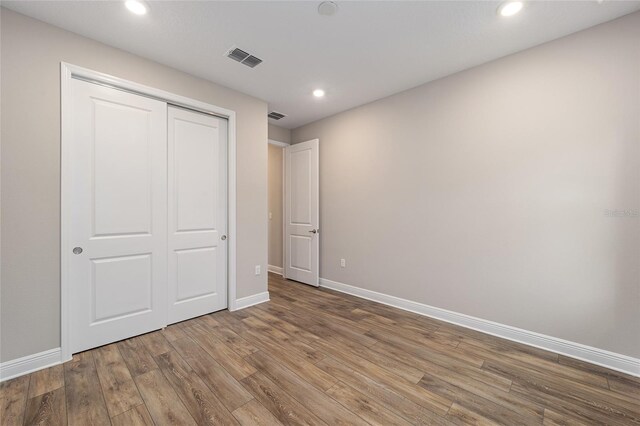 unfurnished bedroom featuring baseboards, visible vents, wood finished floors, a closet, and recessed lighting