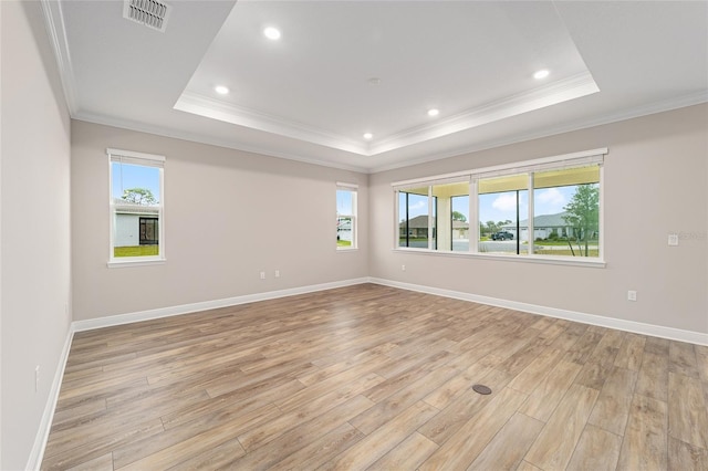 empty room with a raised ceiling, visible vents, light wood-style flooring, and baseboards