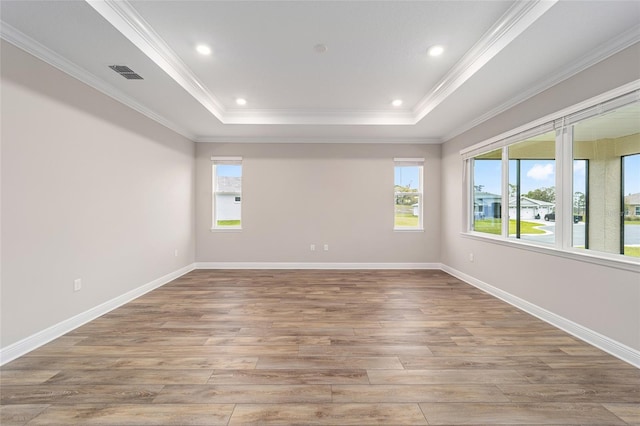 empty room featuring wood finished floors, visible vents, baseboards, a tray ceiling, and crown molding